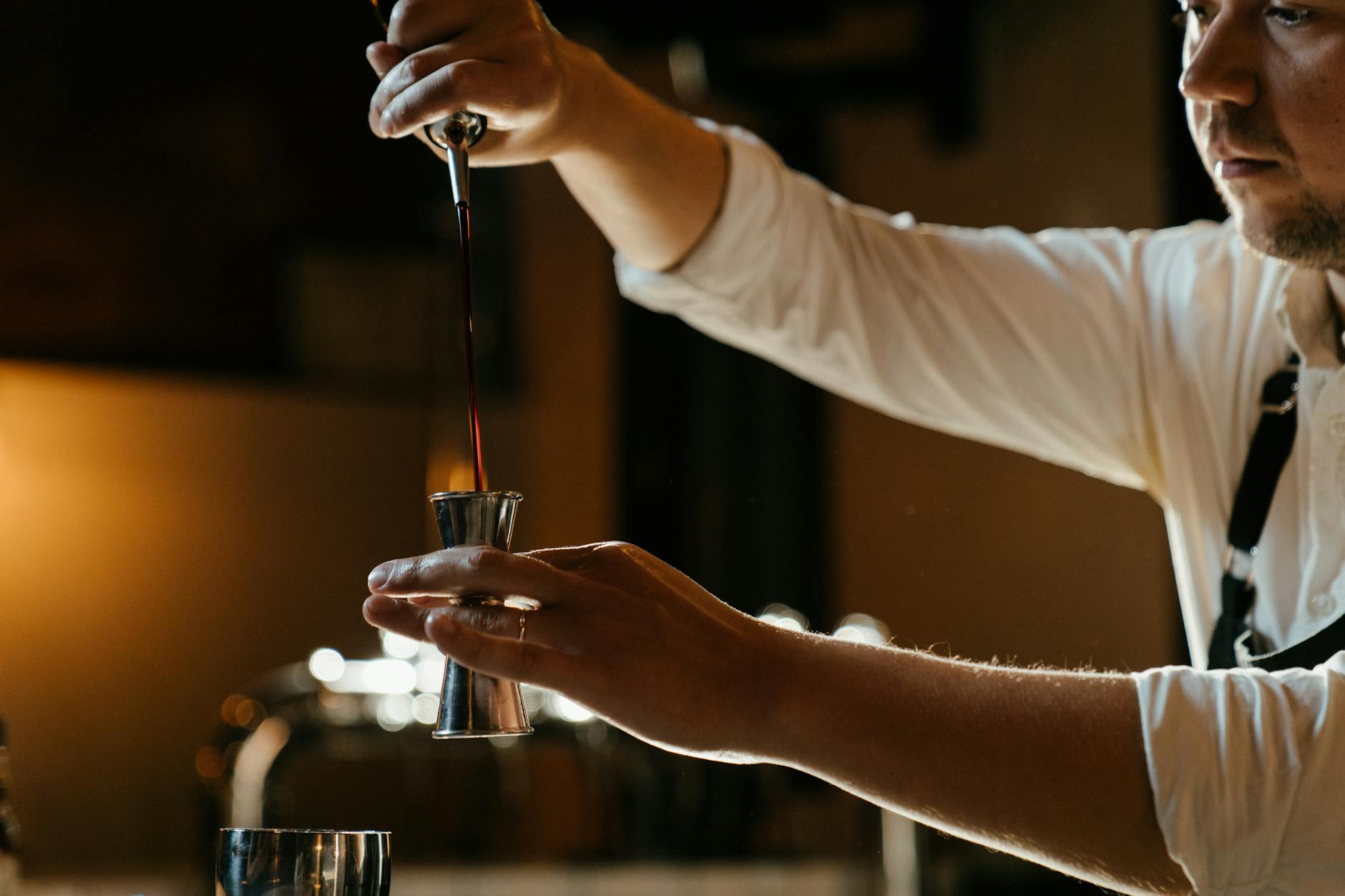 Barman w uniformie odmierza alkohol miarką w przyciemnionym barze